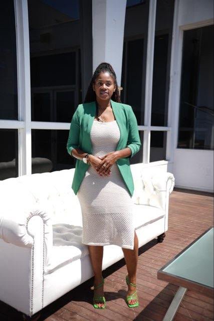 Lovett Love standing on a sunlit deck in a green blazer and white knit dress