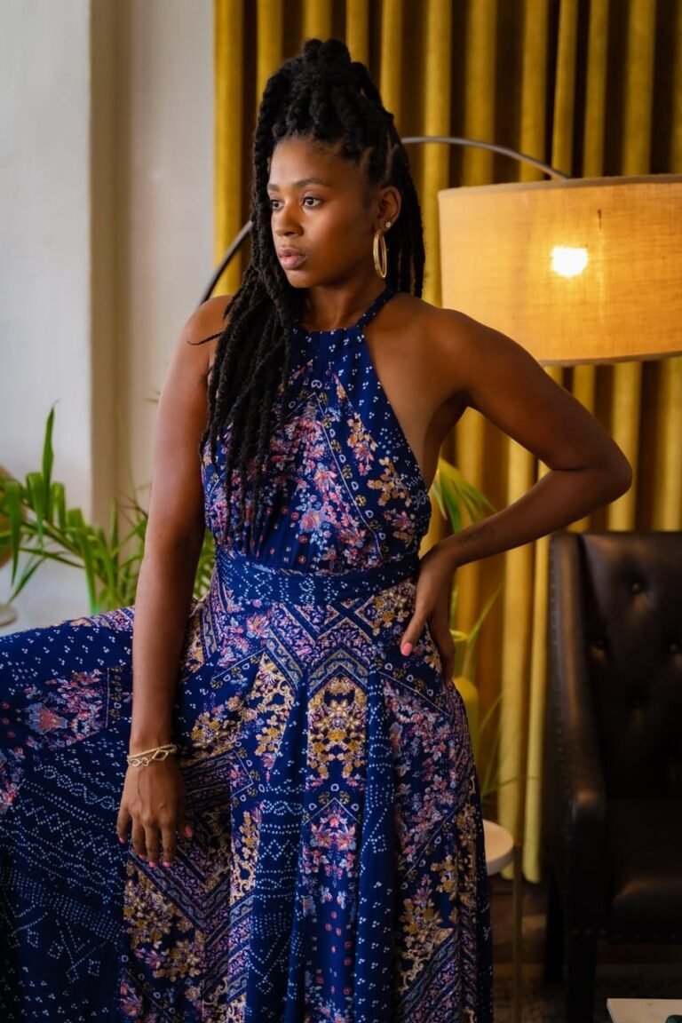 Lovett Love in a blue patterned halter dress beside a warm lamp and gold curtains