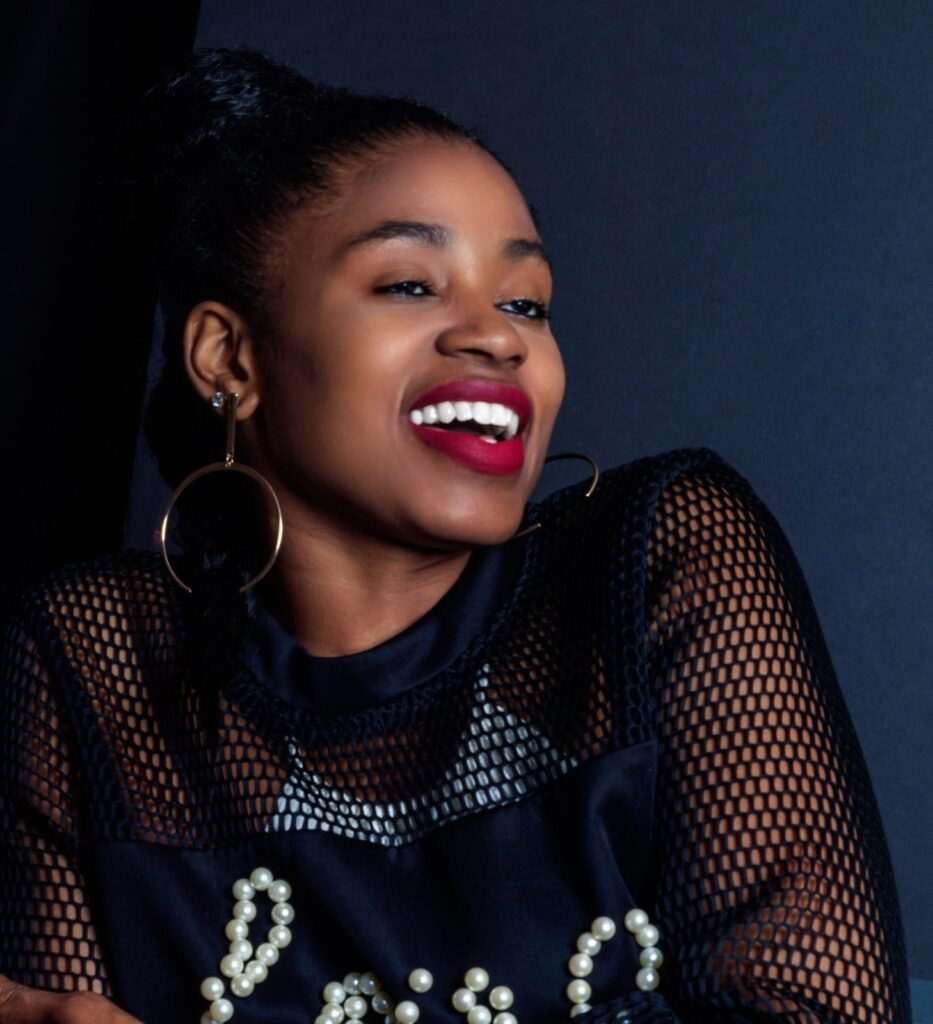 Lovett Love laughing in a black mesh top against a navy backdrop