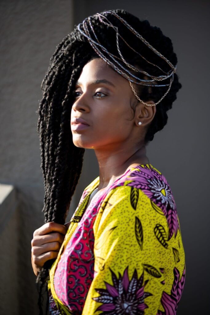 Lovett Love in profile wearing a bright yellow and pink print, holding her braids
